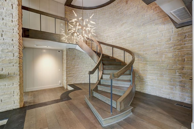 stairs with a high ceiling, wood-type flooring, a chandelier, and visible vents
