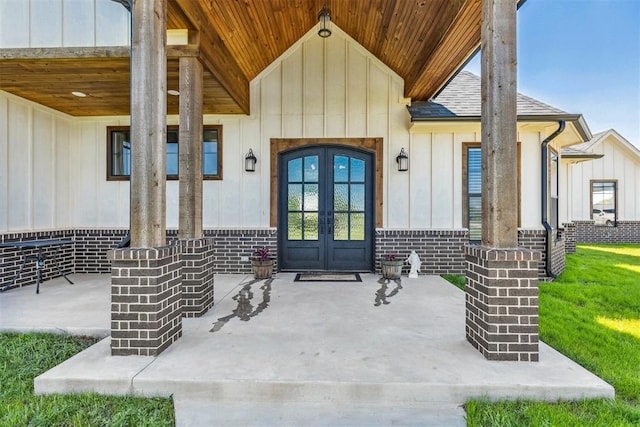 entrance to property with board and batten siding, brick siding, roof with shingles, and french doors