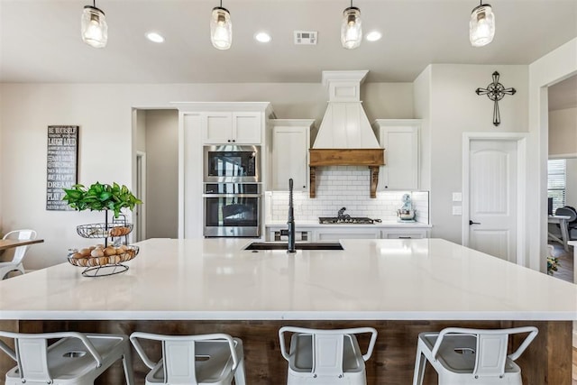 kitchen with a sink, white cabinets, visible vents, tasteful backsplash, and custom range hood