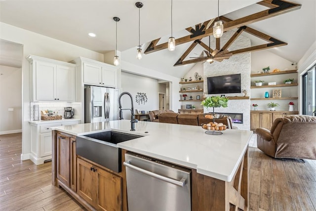kitchen with a sink, open floor plan, lofted ceiling with beams, a fireplace, and appliances with stainless steel finishes