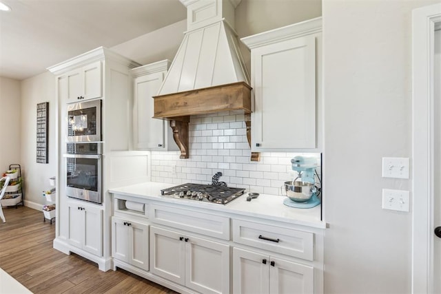 kitchen featuring stainless steel appliances, custom exhaust hood, white cabinetry, light countertops, and tasteful backsplash