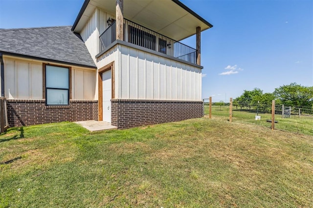 back of house with a balcony, board and batten siding, roof with shingles, and brick siding
