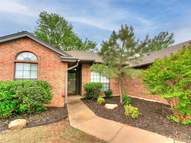 view of front of property featuring brick siding and roof with shingles