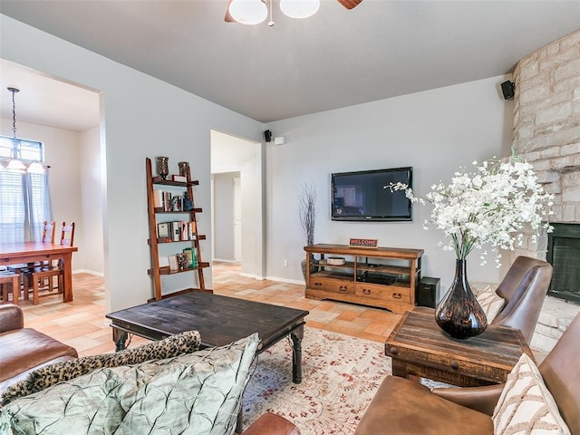 living room with baseboards, a fireplace, and ceiling fan with notable chandelier