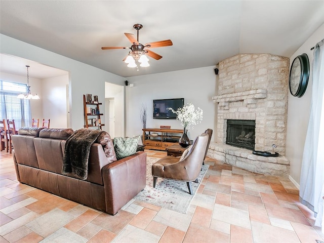living room featuring a stone fireplace, stone finish floor, and ceiling fan with notable chandelier