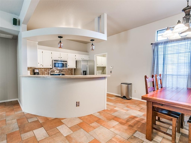 kitchen with a peninsula, white cabinets, stone finish flooring, appliances with stainless steel finishes, and backsplash