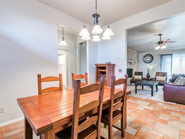 dining space with a stone fireplace, baseboards, ceiling fan with notable chandelier, and stone finish floor