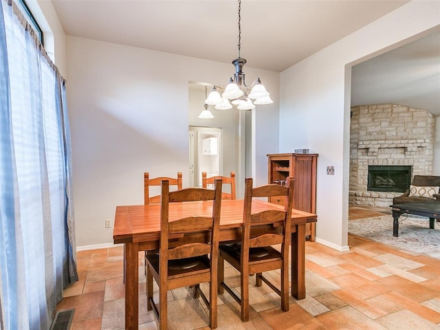 dining space featuring an inviting chandelier, visible vents, baseboards, a stone fireplace, and stone finish floor