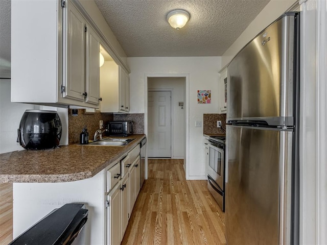 3800 Southwind Ct, Oklahoma City, OK 73179 - kitchen featuring appliances with stainless steel finishes, light wood-style floors, decorative backsplash, a textured ceiling, and dark countertops