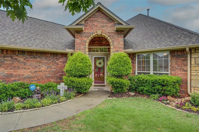 property entrance featuring a yard, brick siding, and roof with shingles
