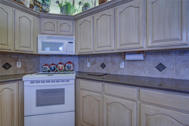 kitchen featuring dark countertops, backsplash, cream cabinets, and white appliances