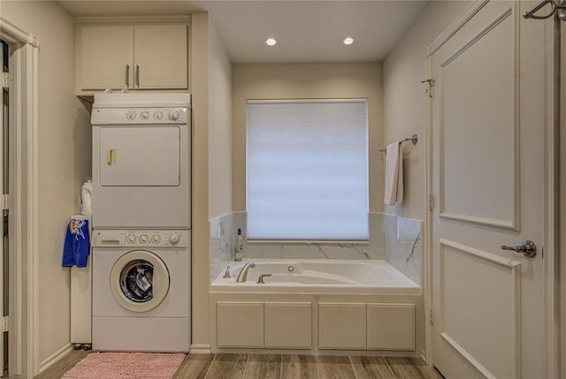 full bathroom featuring a garden tub, recessed lighting, stacked washer / dryer, and wood finished floors