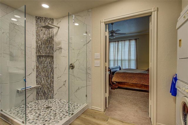 ensuite bathroom featuring ceiling fan, wood finished floors, a marble finish shower, stacked washer and clothes dryer, and ensuite bath