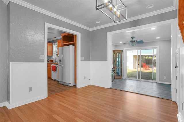 unfurnished dining area with a sink, light wood-type flooring, crown molding, a textured wall, and ceiling fan with notable chandelier