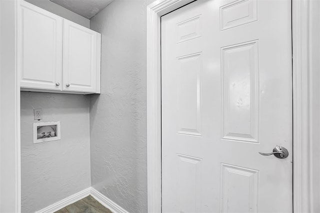washroom featuring cabinet space, a textured wall, washer hookup, and baseboards