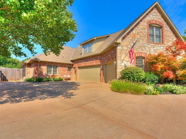 traditional home with concrete driveway, roof with shingles, stone siding, and fence