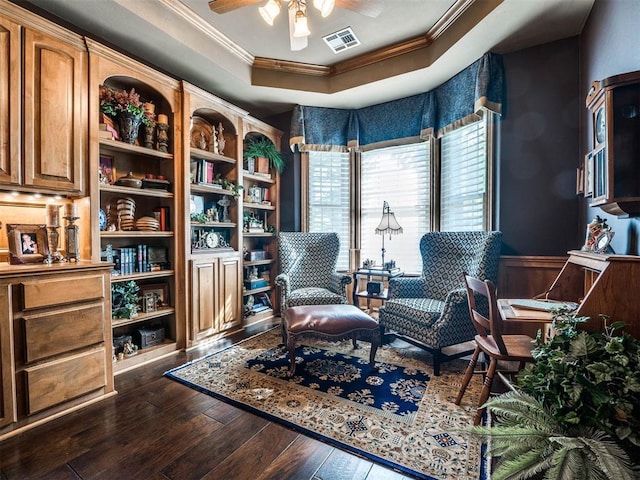 sitting room with a wainscoted wall, ceiling fan, dark wood-style flooring, visible vents, and crown molding