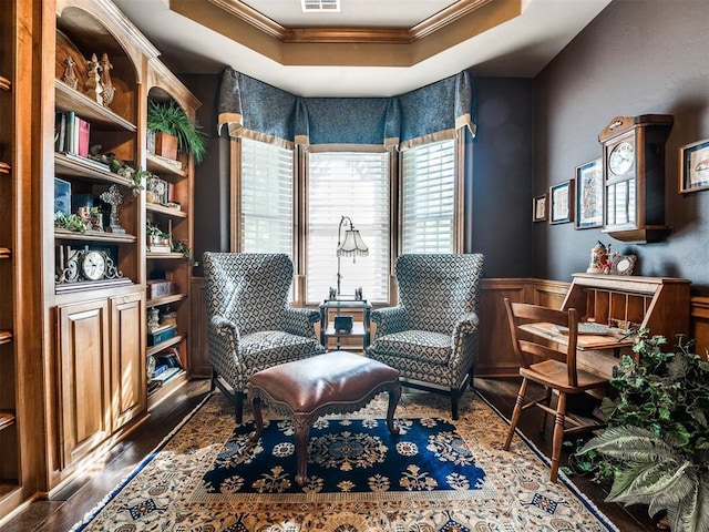 living area featuring wood finished floors, a wainscoted wall, visible vents, crown molding, and a tray ceiling