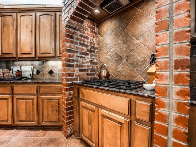 kitchen featuring black gas stovetop, dark stone countertops, brown cabinets, and decorative backsplash