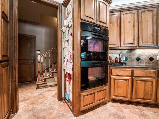 kitchen featuring tasteful backsplash, dobule oven black, brown cabinetry, and dark stone counters