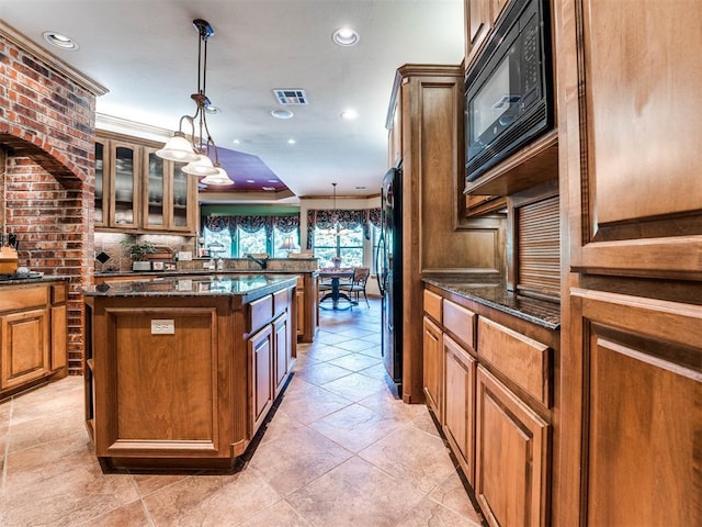 kitchen featuring black appliances, dark stone countertops, a kitchen island, and brown cabinetry