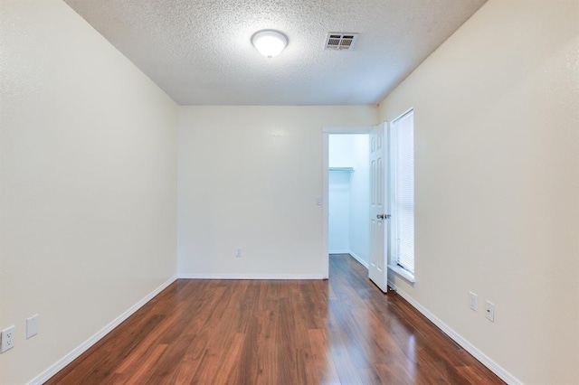 empty room with a textured ceiling, visible vents, dark wood-style flooring, and baseboards