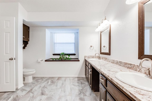 full bath featuring toilet, double vanity, a sink, and marble finish floor