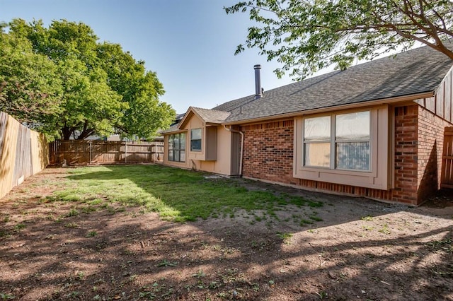 rear view of property with a lawn, roof with shingles, a fenced backyard, and brick siding