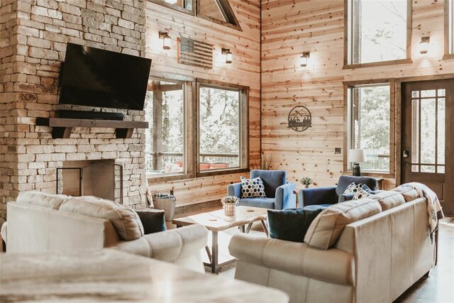 living area featuring wooden walls, a fireplace, a healthy amount of sunlight, and a towering ceiling