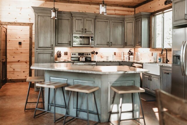 kitchen with a kitchen bar, finished concrete floors, decorative light fixtures, a sink, and stainless steel appliances
