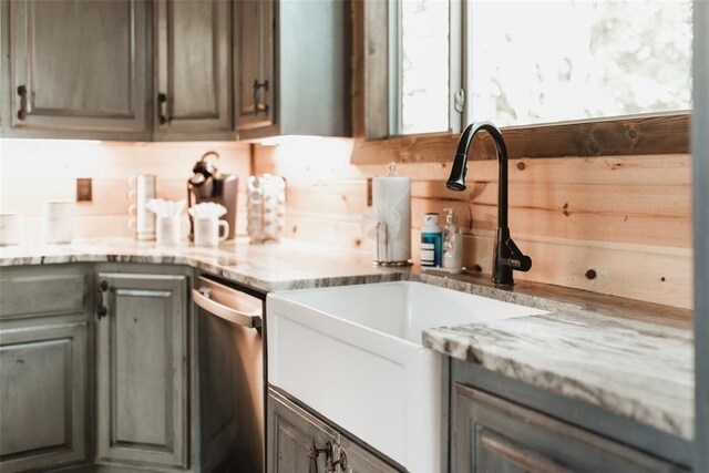 kitchen featuring stainless steel dishwasher, a sink, and light stone countertops