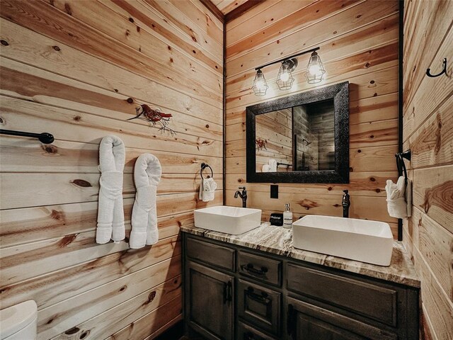 bathroom featuring a sink, toilet, wooden walls, and double vanity