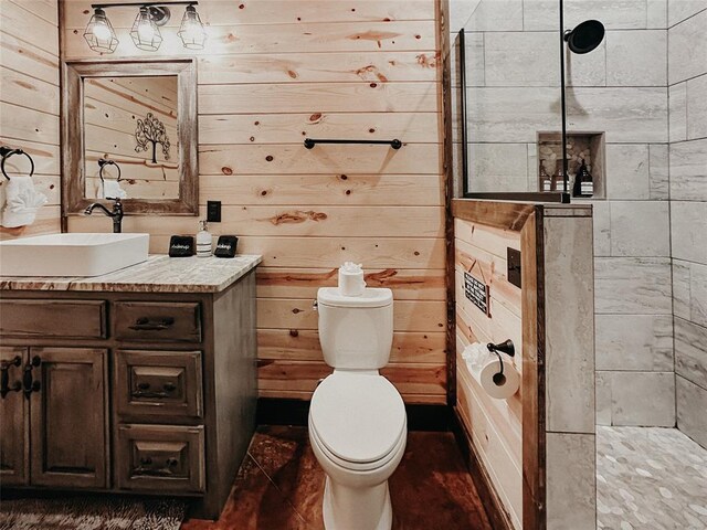 full bath with vanity, toilet, wood walls, and tiled shower