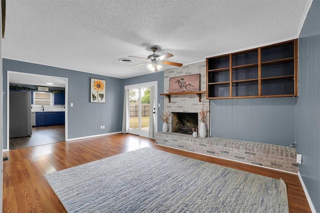 305 S Mockingbird Dr, Altus, OK 73521 - unfurnished living room with a brick fireplace, a ceiling fan, a textured ceiling, and wood finished floors
