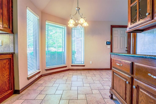 unfurnished dining area featuring baseboards, stone finish flooring, an inviting chandelier, and vaulted ceiling