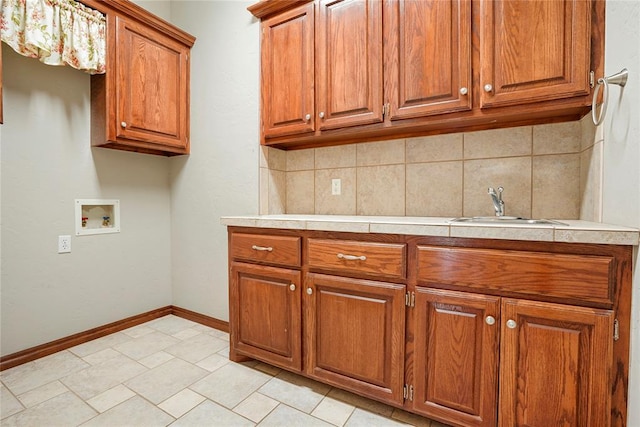 clothes washing area featuring baseboards, hookup for a washing machine, a sink, and cabinet space