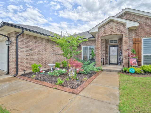 entrance to property with driveway, a shingled roof, an attached garage, and brick siding