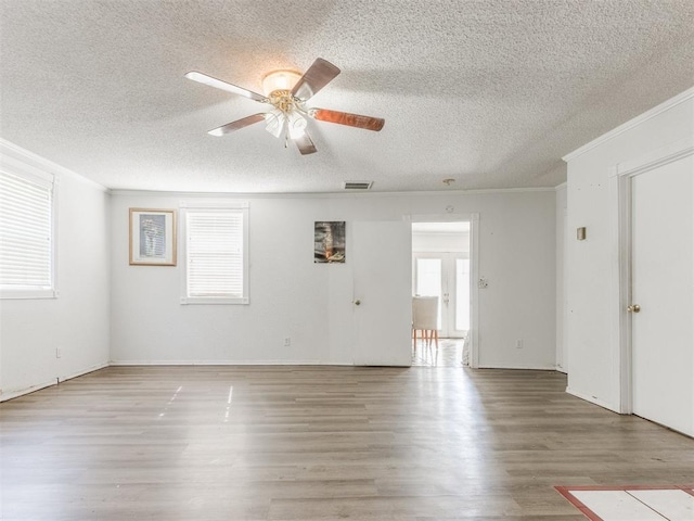 empty room featuring ornamental molding, a textured ceiling, visible vents, and wood finished floors