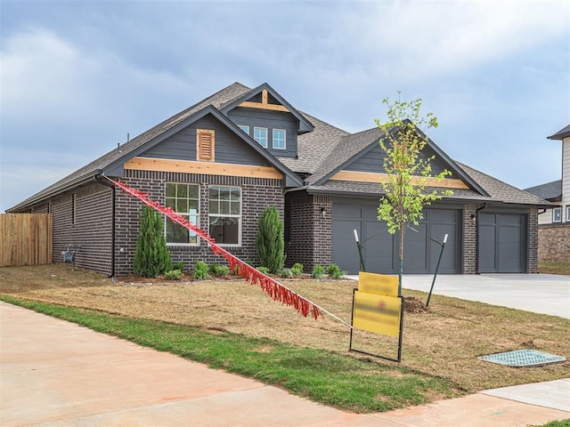 craftsman-style house featuring driveway, roof with shingles, an attached garage, fence, and brick siding