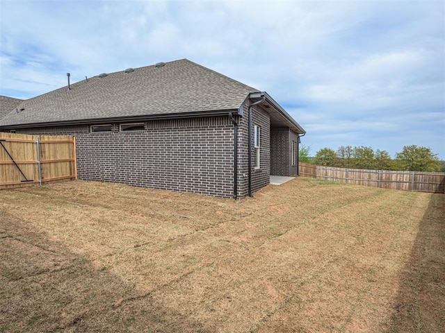 rear view of house with roof with shingles, a yard, brick siding, and a fenced backyard