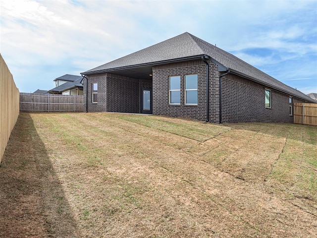 rear view of house with a lawn, roof with shingles, a fenced backyard, and brick siding