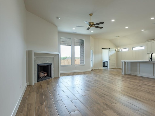 unfurnished living room featuring a sink, a barn door, light wood-type flooring, a ceiling fan, and baseboards