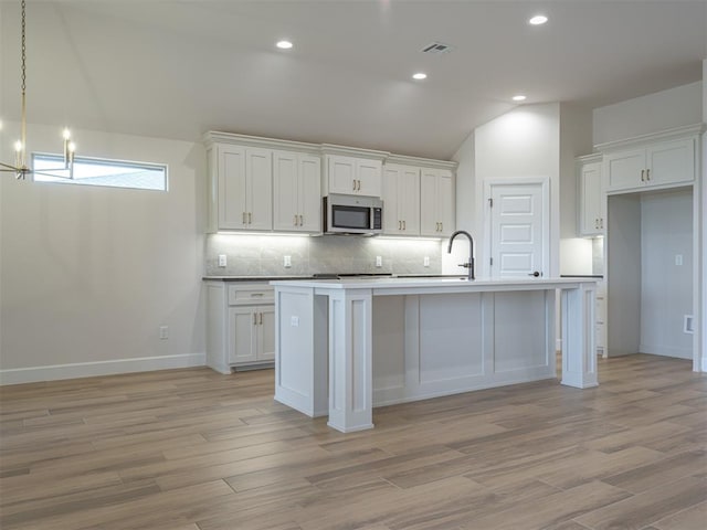 kitchen featuring stainless steel microwave, light wood-type flooring, visible vents, and white cabinets