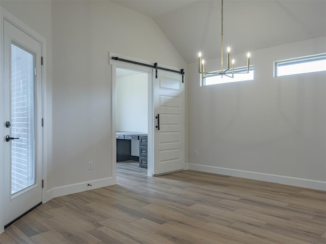 unfurnished dining area with an inviting chandelier, a barn door, wood finished floors, baseboards, and lofted ceiling