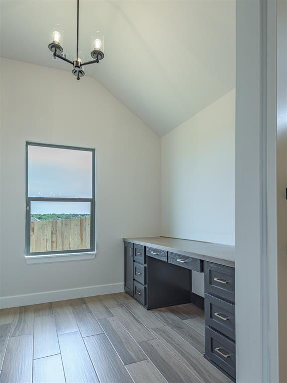unfurnished office featuring lofted ceiling, wood finished floors, a chandelier, and baseboards