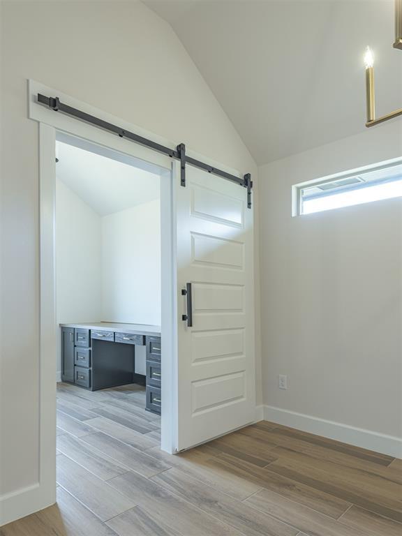 interior space featuring baseboards, a barn door, light wood-type flooring, and lofted ceiling