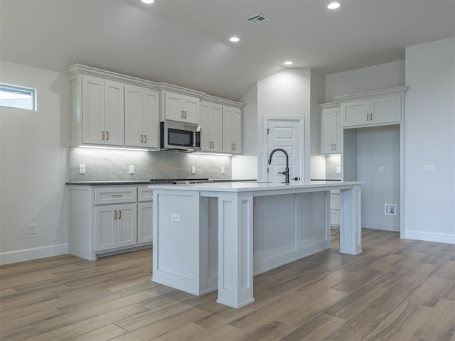 kitchen featuring visible vents, decorative backsplash, light wood-style flooring, and stainless steel microwave