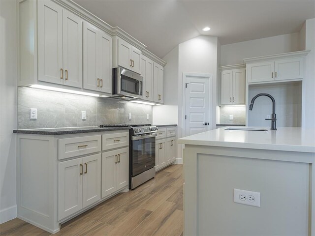 kitchen with lofted ceiling, a sink, appliances with stainless steel finishes, light wood finished floors, and backsplash