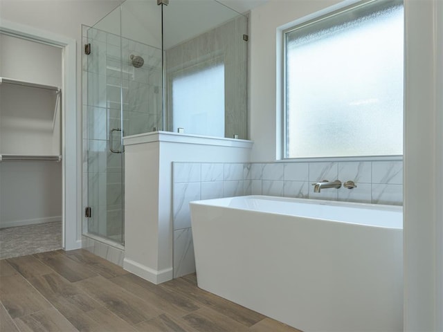 bathroom with a freestanding tub, wood finished floors, a shower stall, and a walk in closet