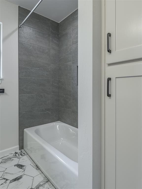 bathroom with baseboards, washtub / shower combination, and marble finish floor